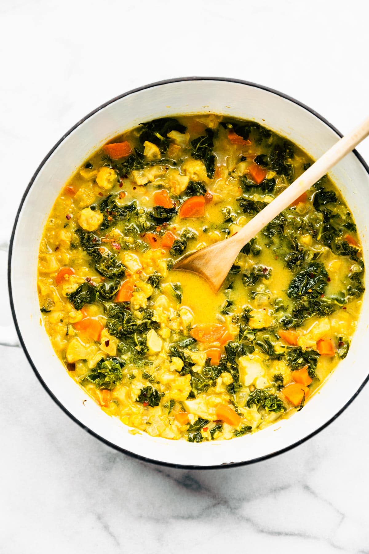 A pot of Curried Cauliflower Soup with Kale being stirred with a wooden spoon.