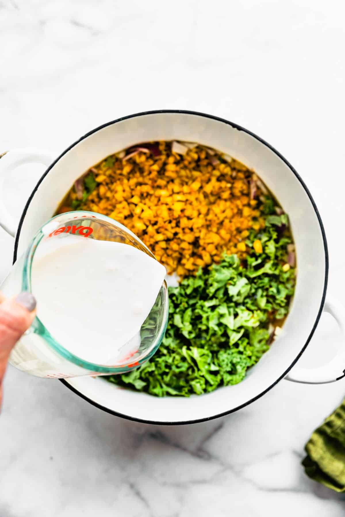Coconut milk being poured on top of vegetables in a pot.