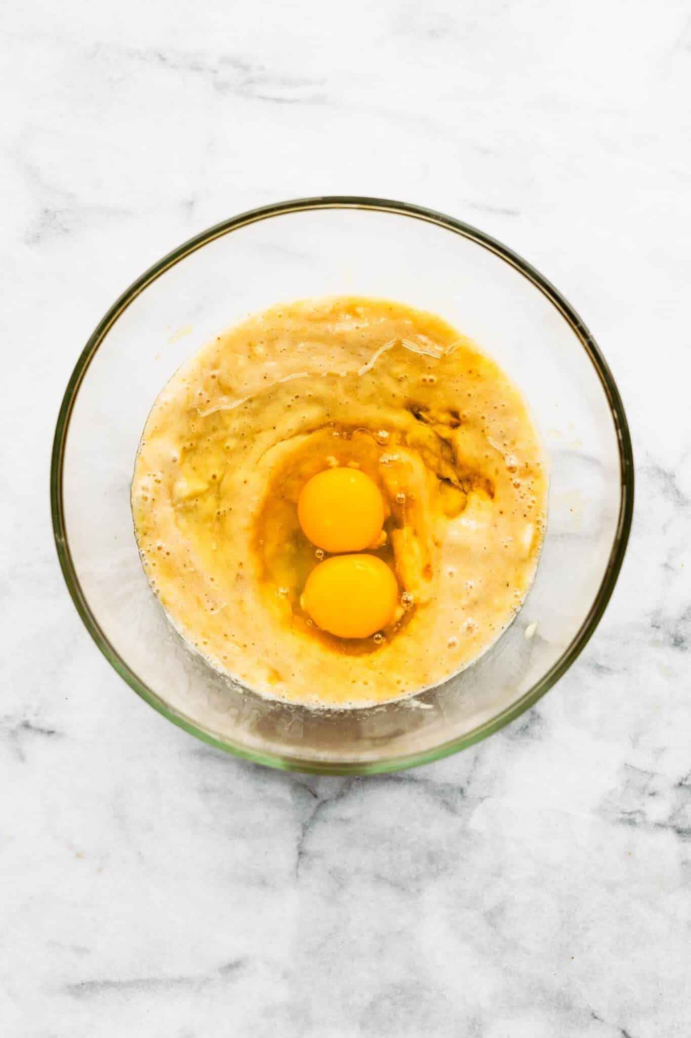 Two eggs in the wet ingredients in a glass mixing bowl.