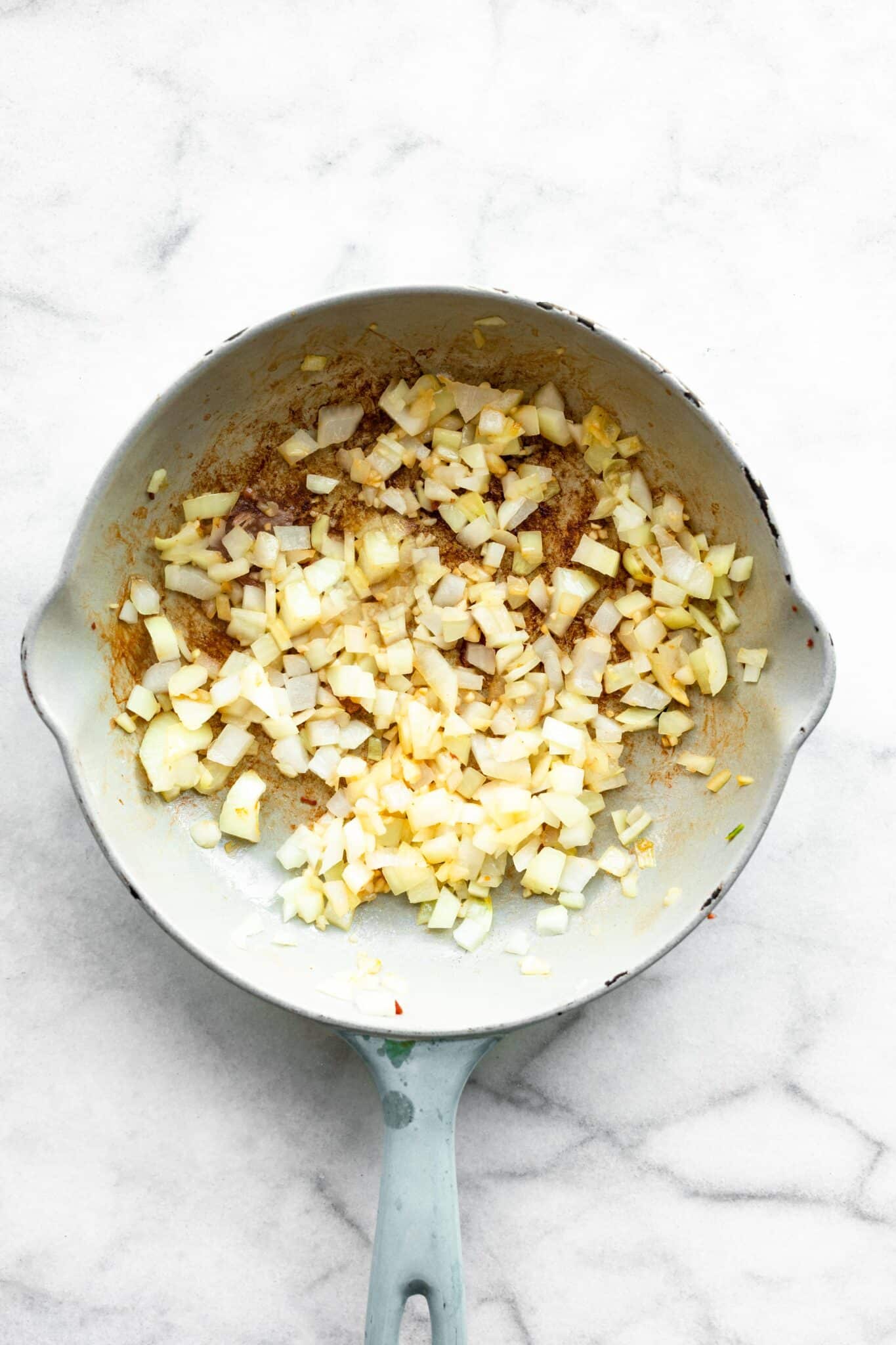 Overhead photo of a glazed cast iron pan with diced onion and garlic.