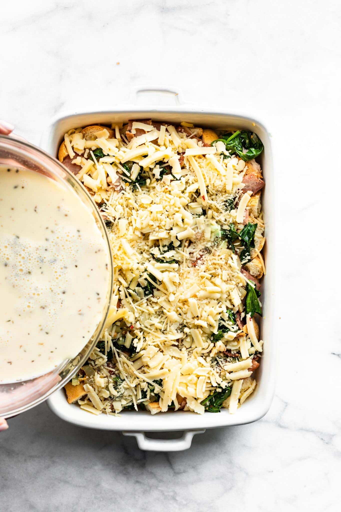 A bowl of egg mixture being poured into a pan of gluten free breakfast strata.