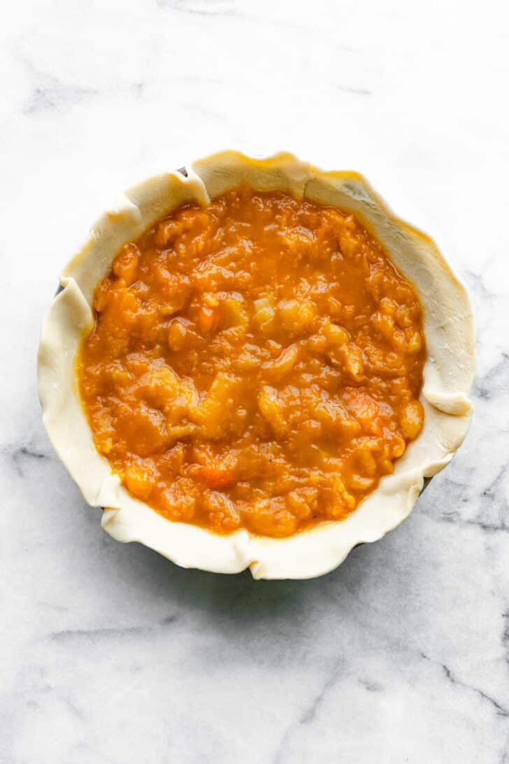 Apricot pie filling spread in an unbaked pie crust, set in a clear glass pie pan.