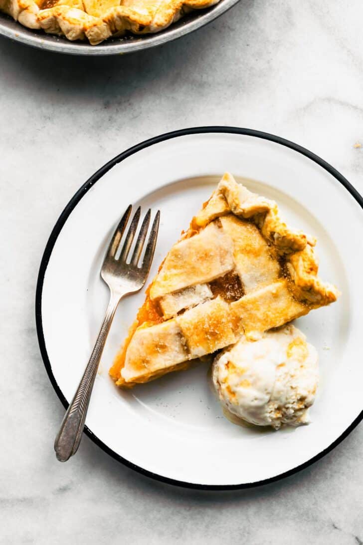A slice of apricot pie on a plate with a fork, served with a scoop of ice cream on the side.