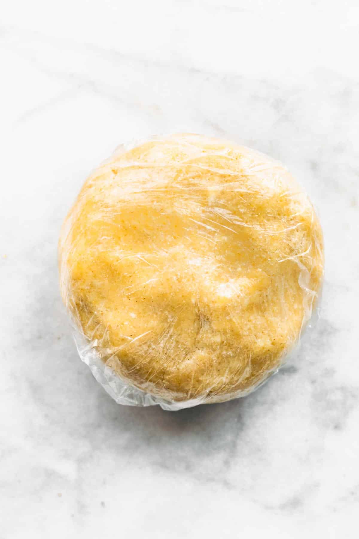 Gluten free pie dough puck in clear plastic wrap.