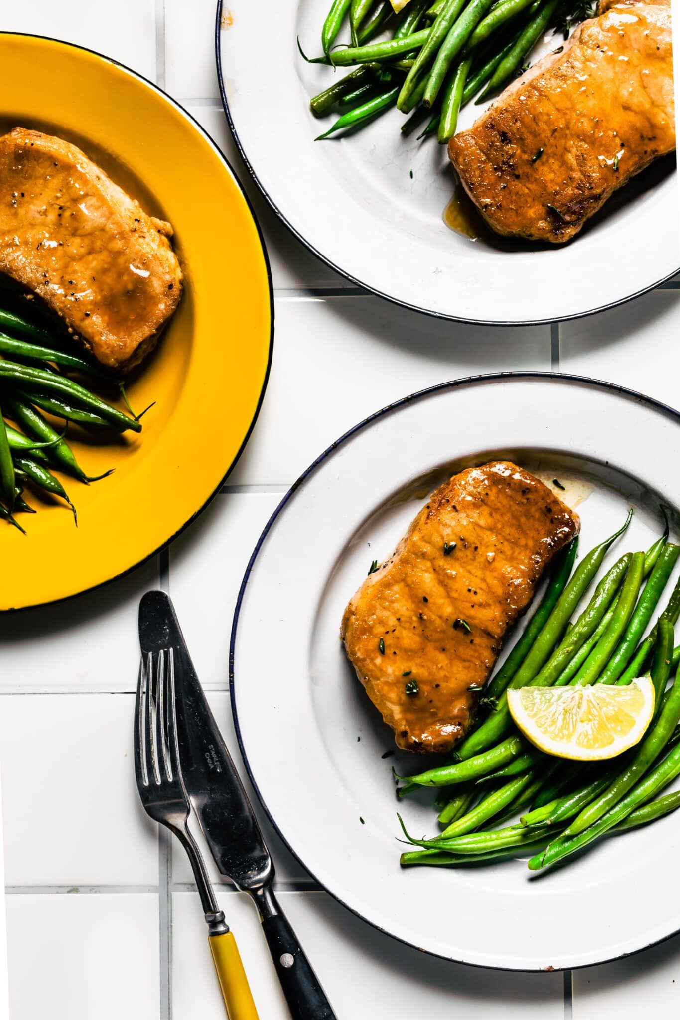 Overhead photo of three plates of glazed pork chops with a side of green beans.