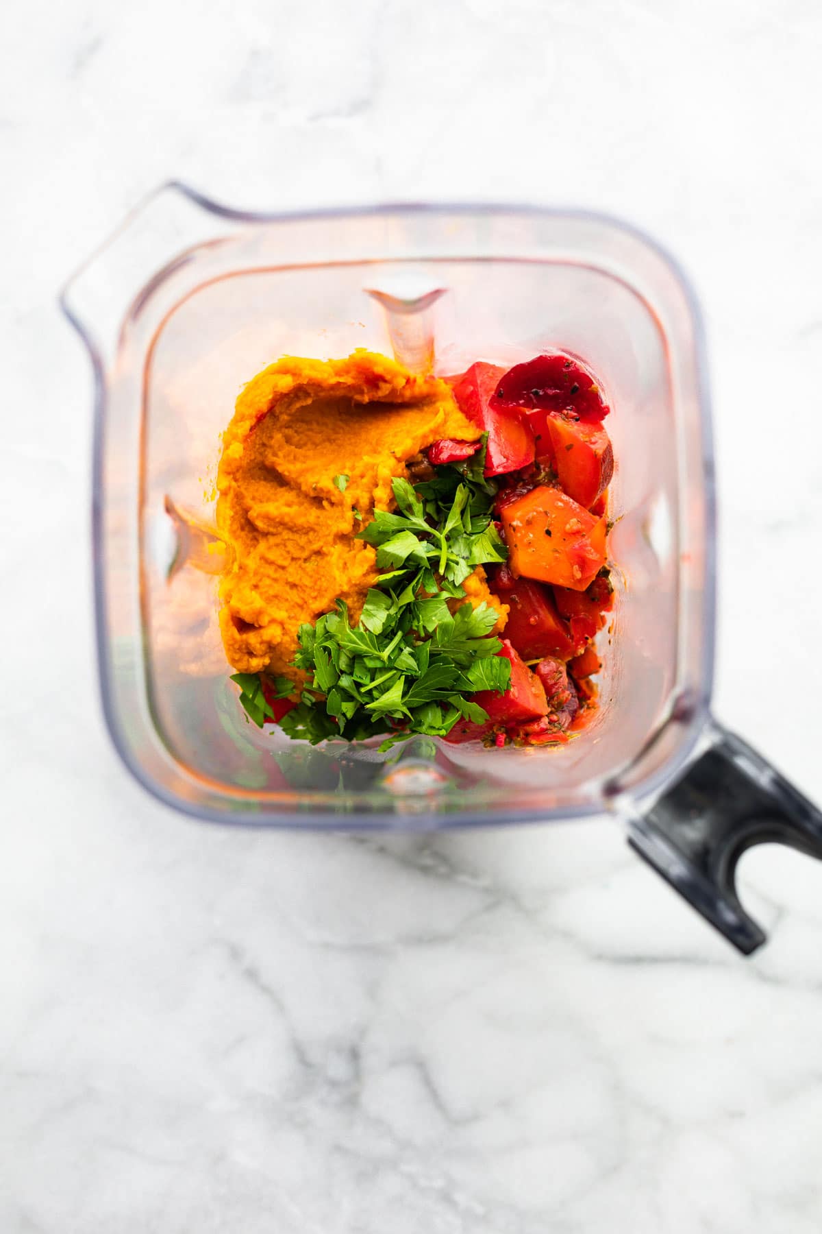 An overhead photo of cooked beets, vegetables, and herbs in a blender.