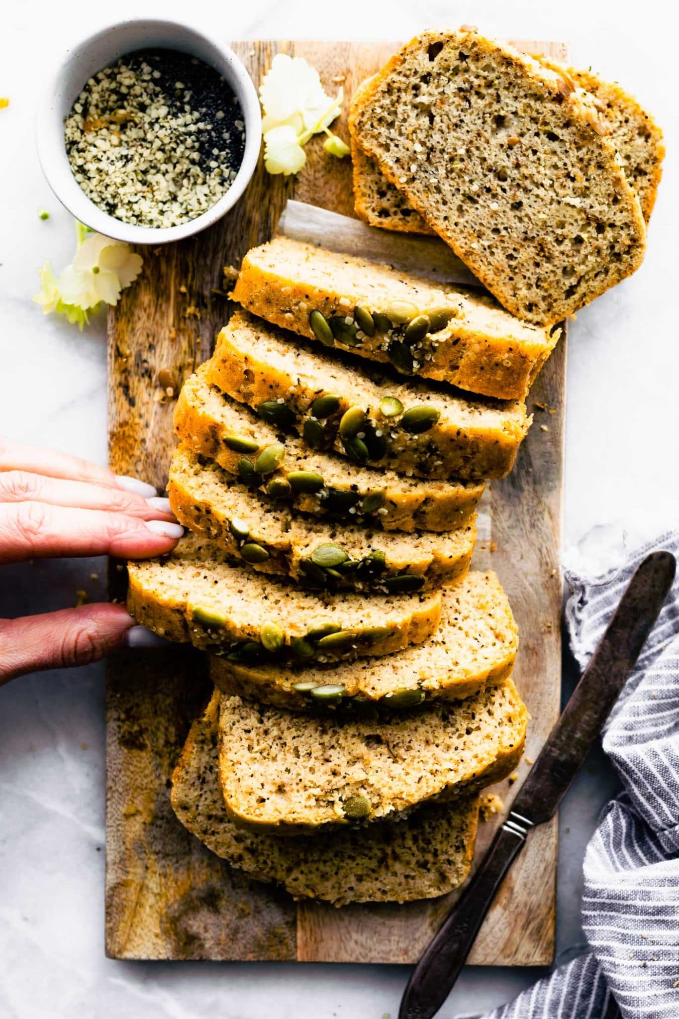 A woman's hand reaching for a slice of grain free bread on a cutting board.