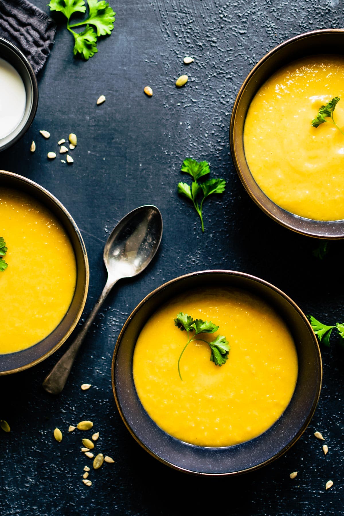3 bowls of soup with a spoon on the side on a dark countertop.