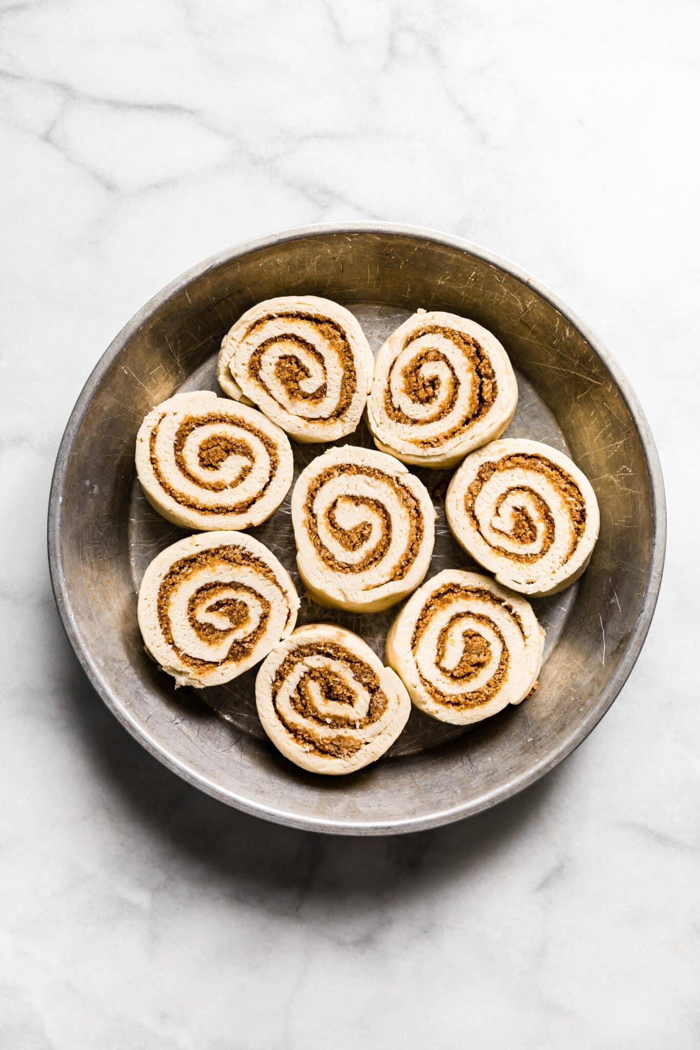gluten free cinnamon roll dough rolled up and cut into rolls unbaked in a metal pan