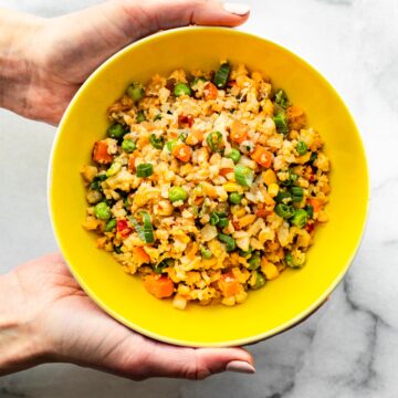 Hands holding a bowl of Cauliflower Fried Rice.
