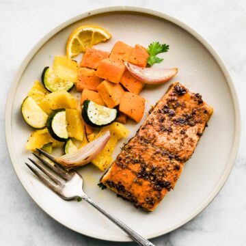 An overhead view of a white plate with baked jerk salmon and roasted veggies.