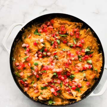 Baked chicken fajita casserole in skillet, topped with melted cheese, diced tomatoes, and cilantro.