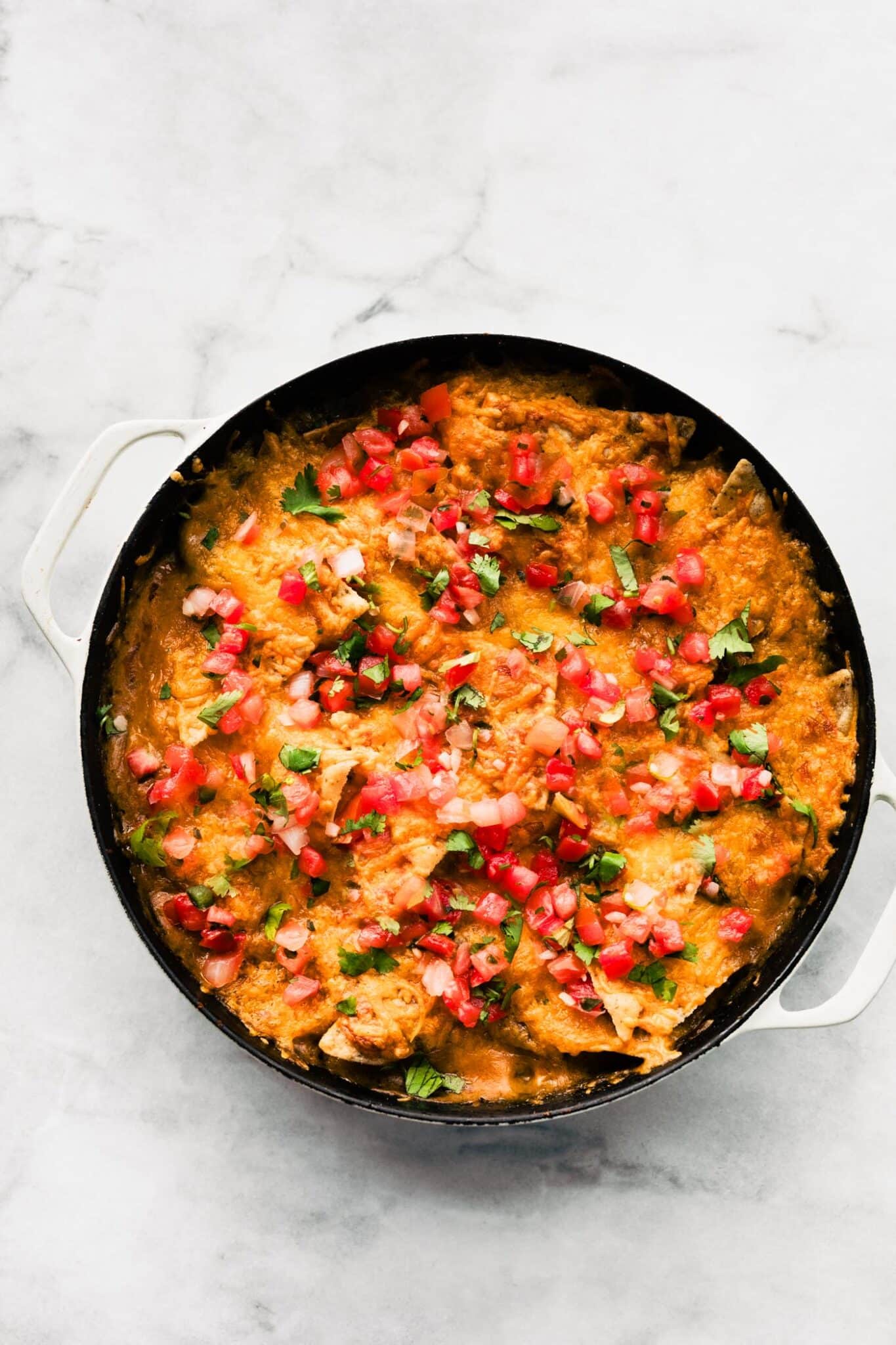 Baked chicken fajita casserole in skillet, topped with melted cheese, diced tomatoes, and cilantro.