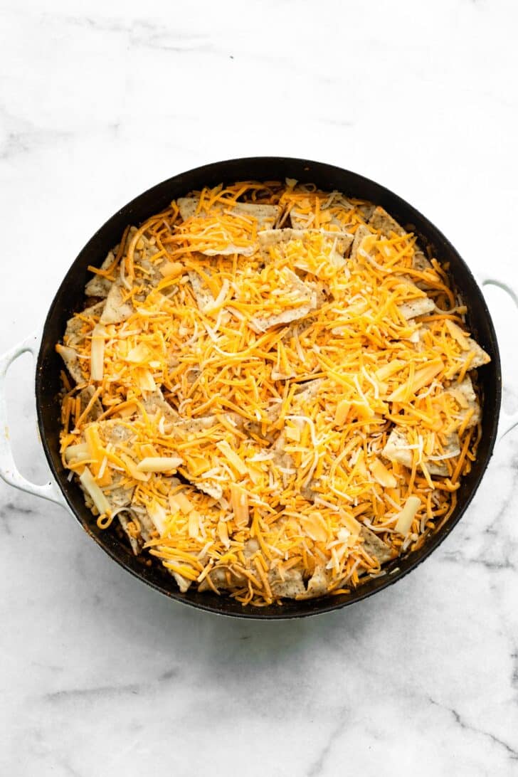 Casserole skillet layered with tortilla chips and shredded cheese before baking.
