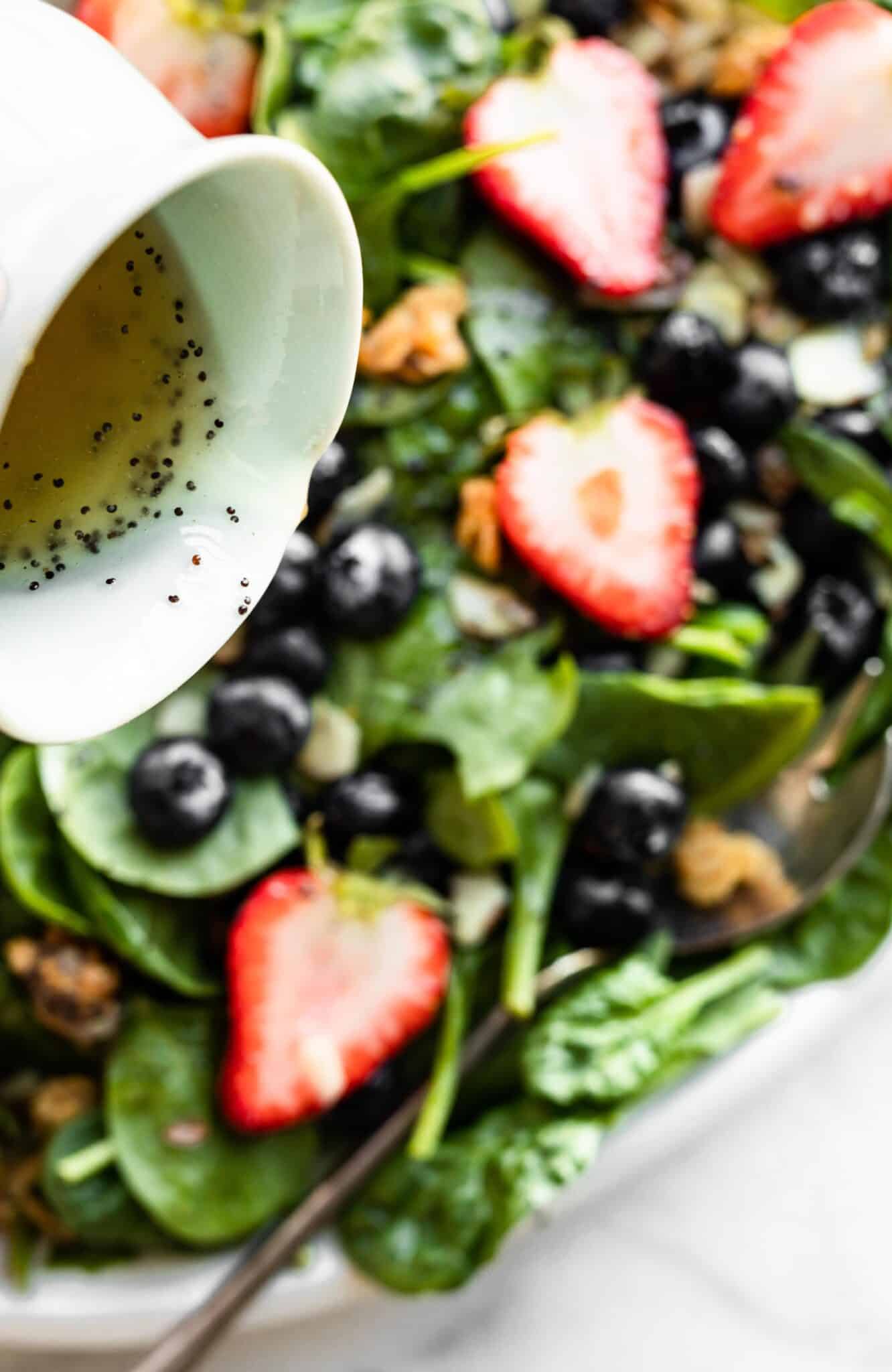 A poppyseed dressing being poured over a strawberry spinach salad.