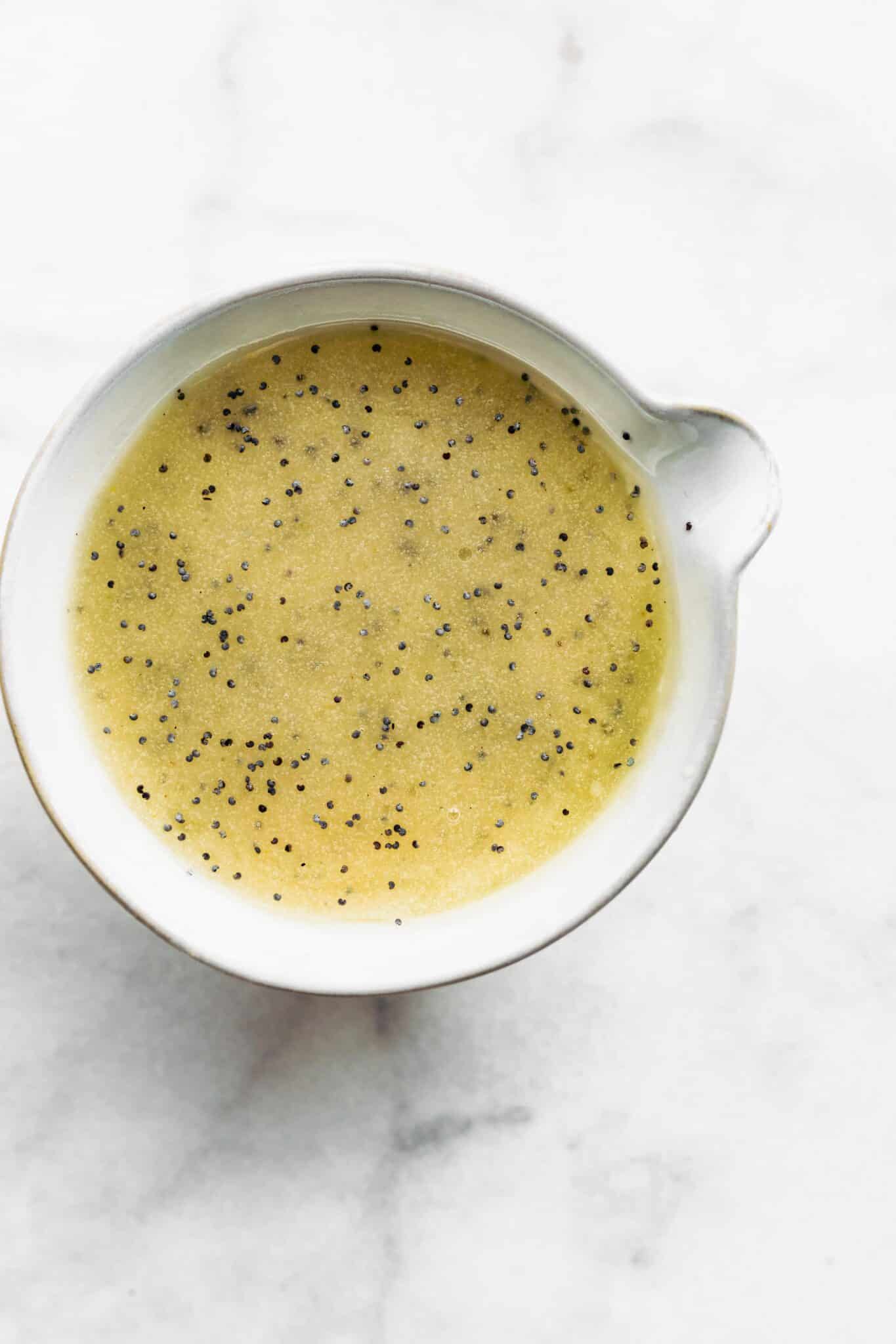 Overhead photo of a poppyseed salad dressing in a white dish on a marble countertop.