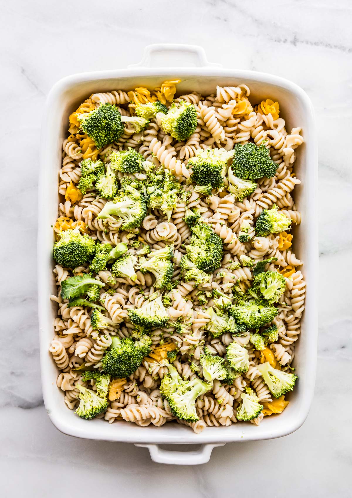 Overhead shot of broccoli being layered on top of pasta