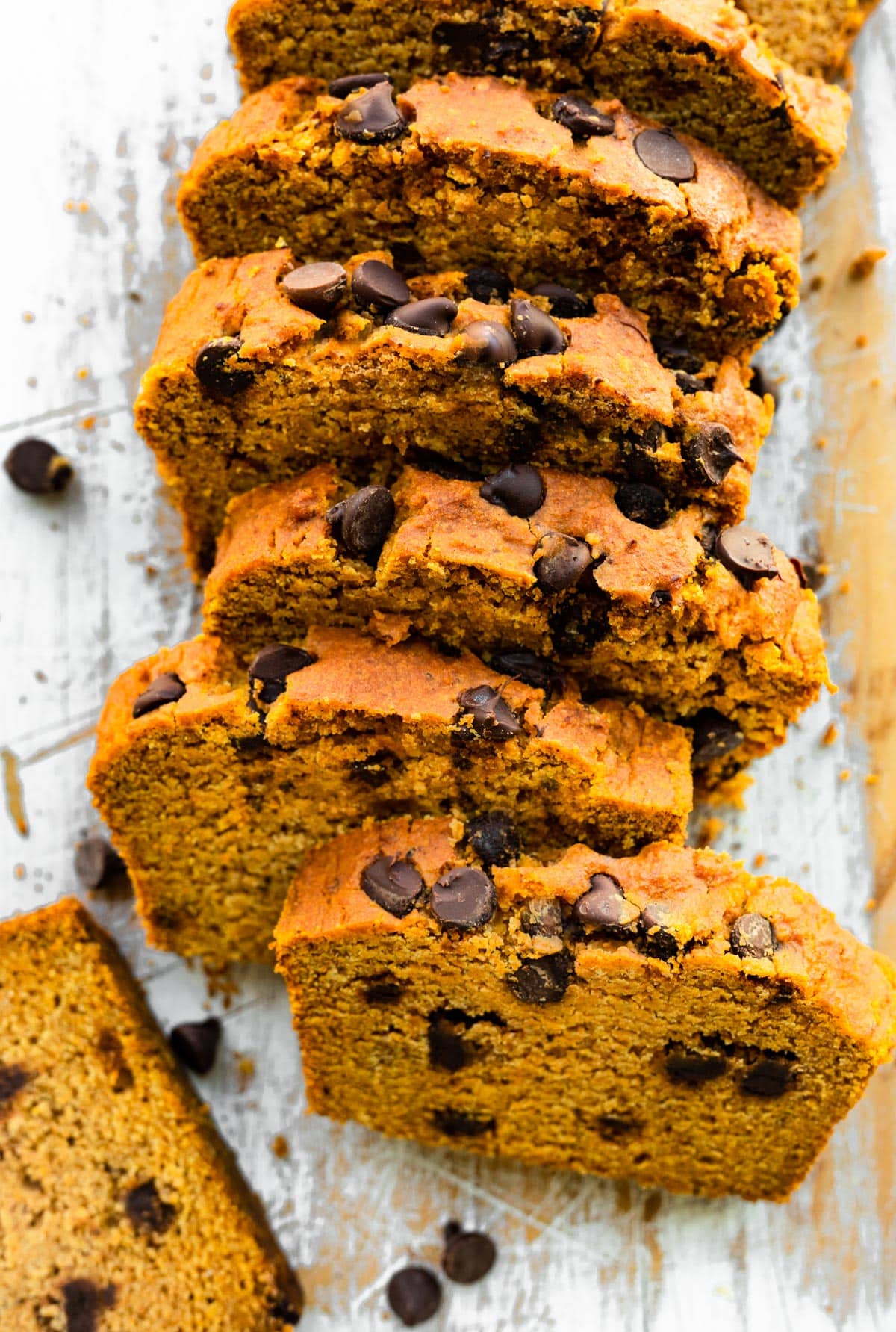 Overhead photo of sliced vegan pumpkin bread on a white wooden cutting board.
