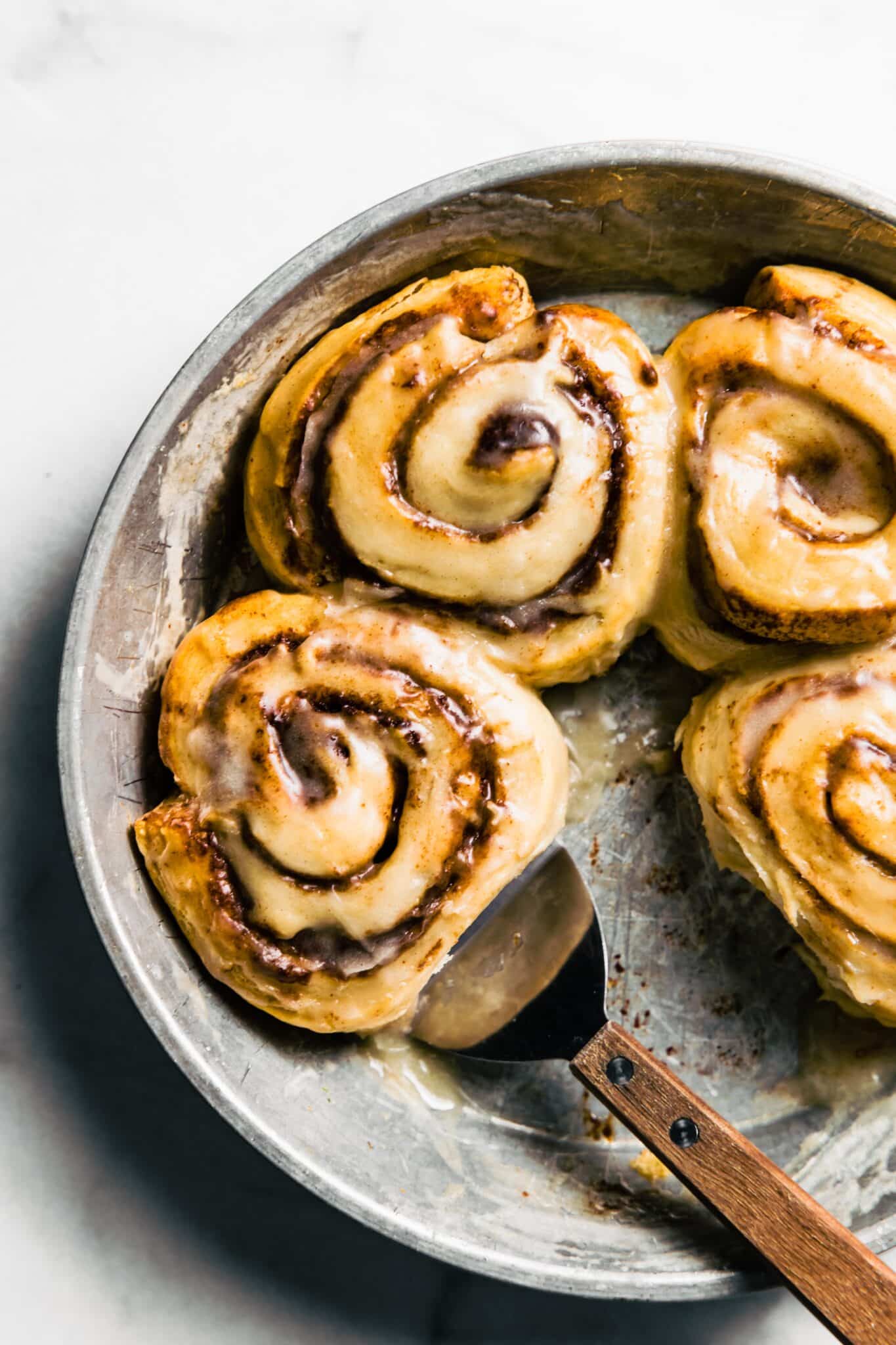 pan of gluten free cinnamon rolls baked with icing and metal spatula to underneath one