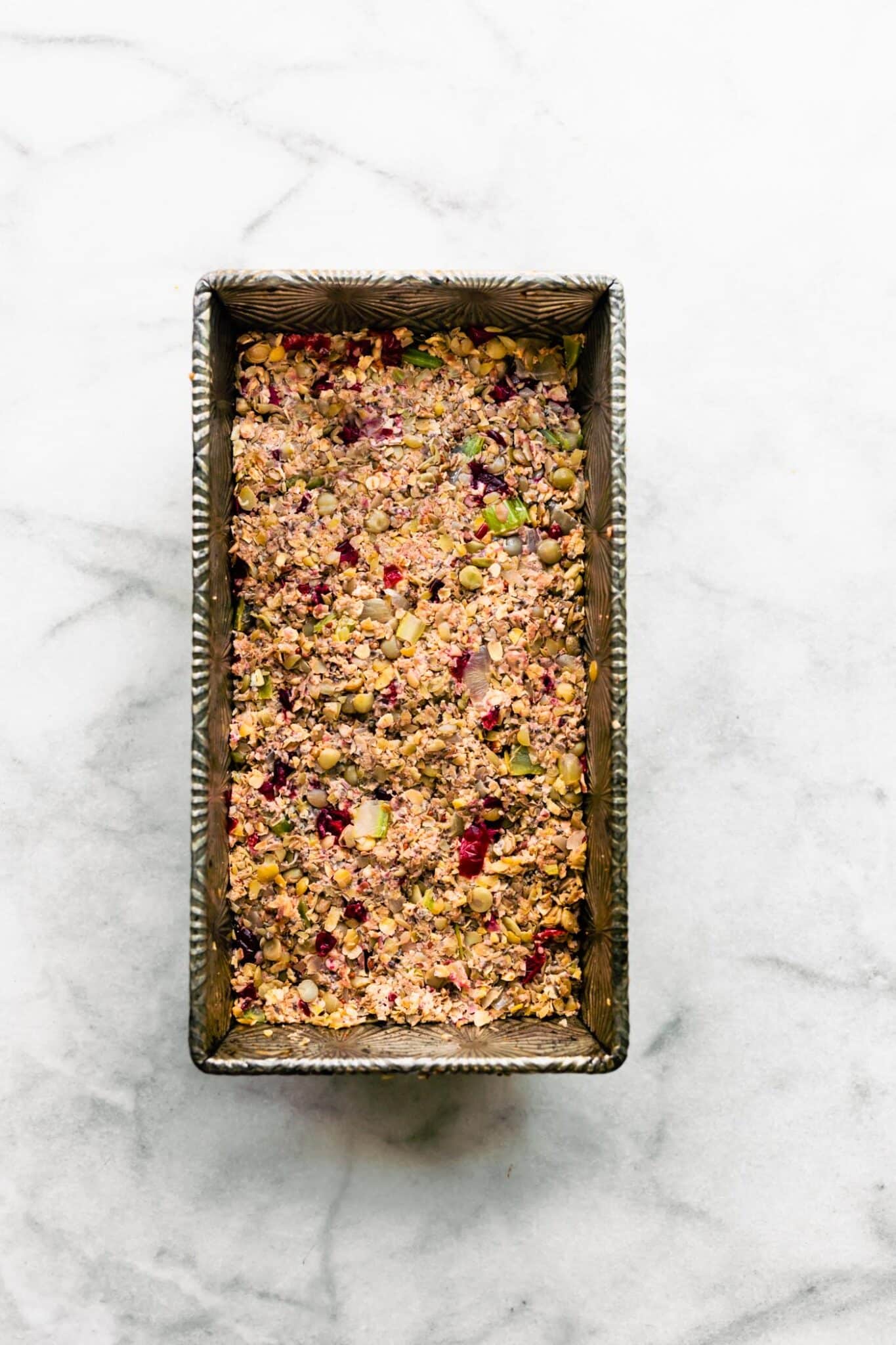 Overhead photo of an unbaked lentil loaf pressed into a metal bread pan.