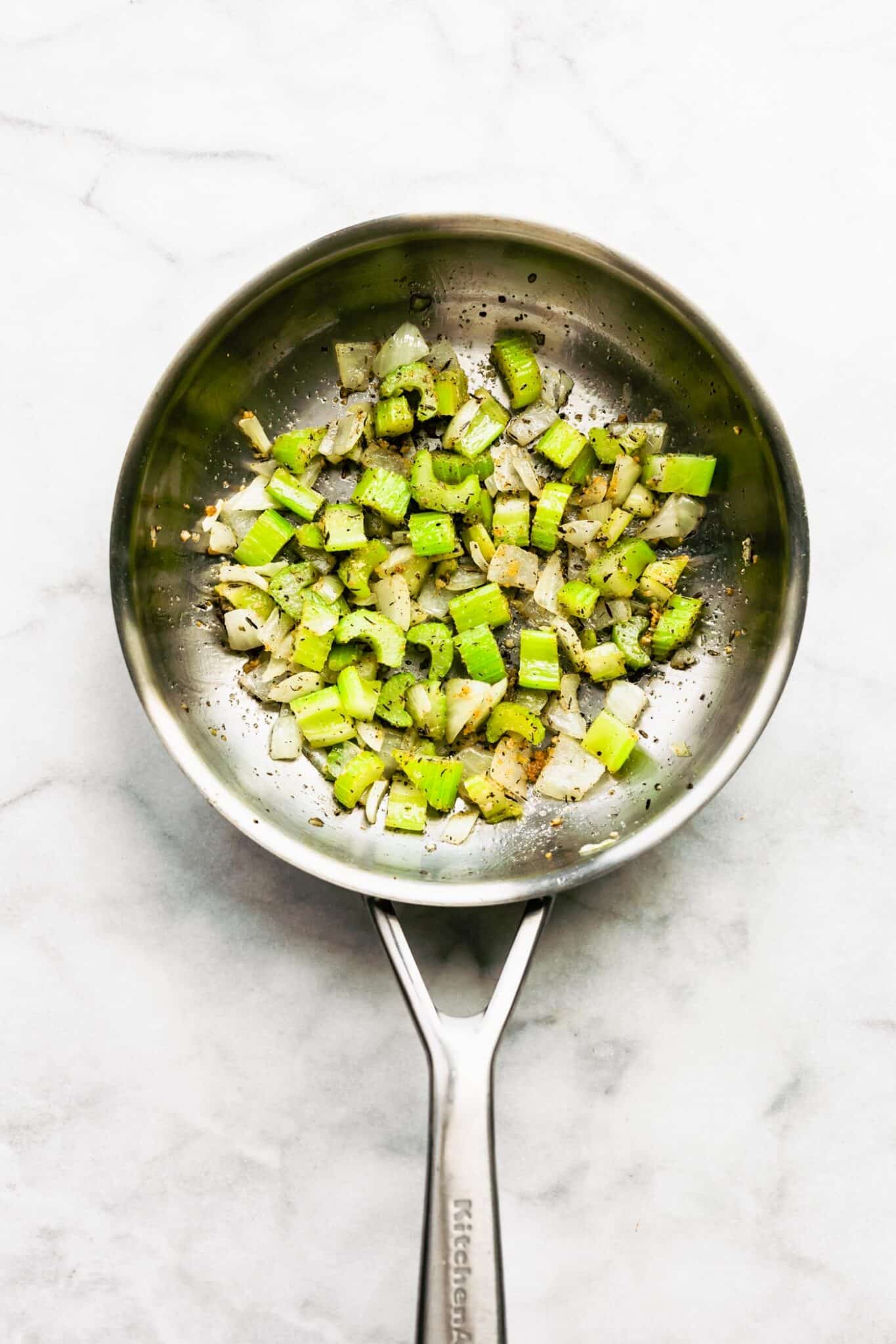 Overhead photo of onions and celery sauteed in a metal pan.