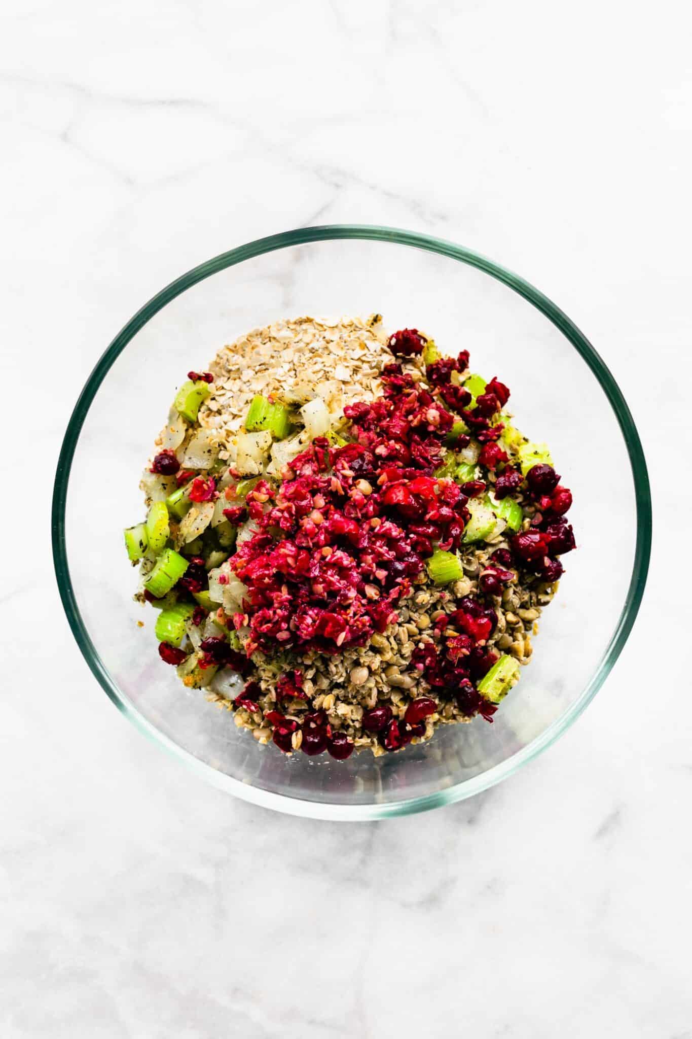 Overhead photo of diced cranberries, celery, oats, and cooked lentils in a glass bowl.