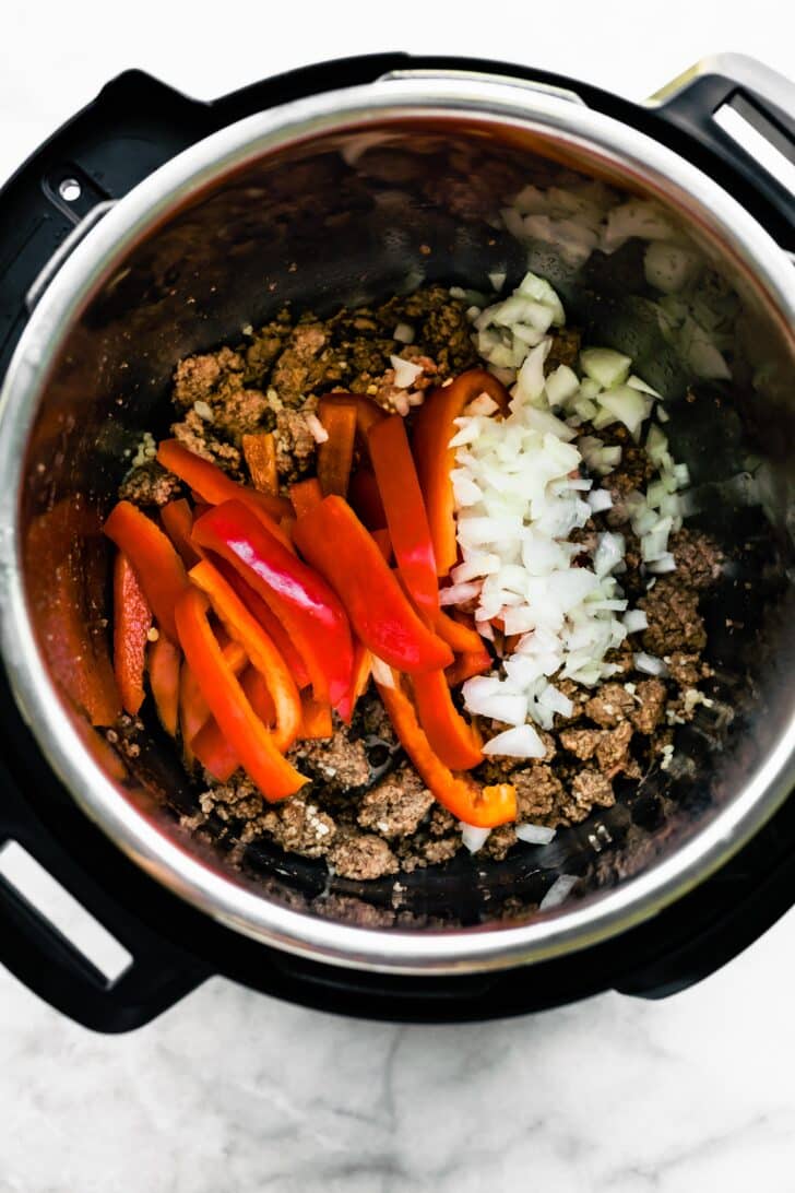 Overhead photo of red bell pepper slices and onion over browned ground beef.