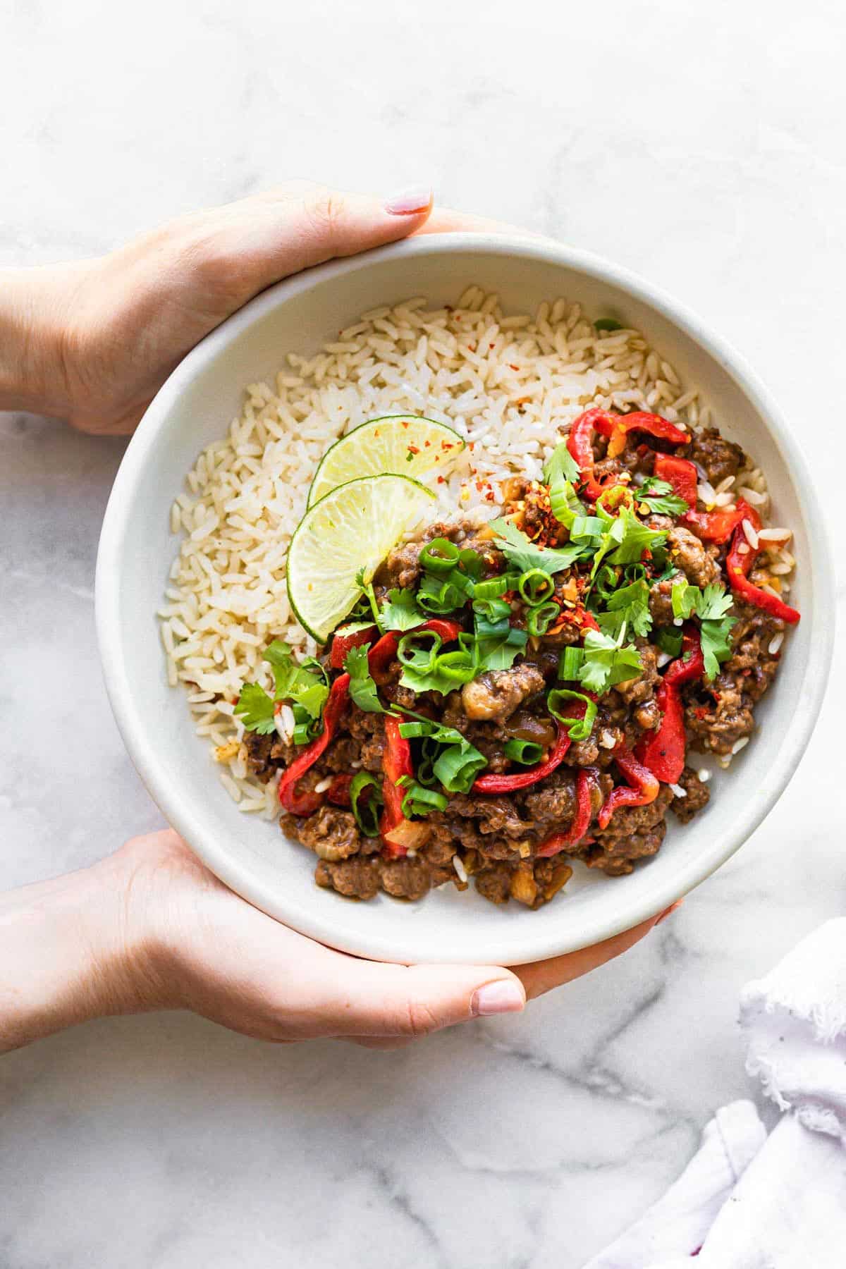 A woman's hands holding a bowl of rice with beef bulgogi topped with green onion.