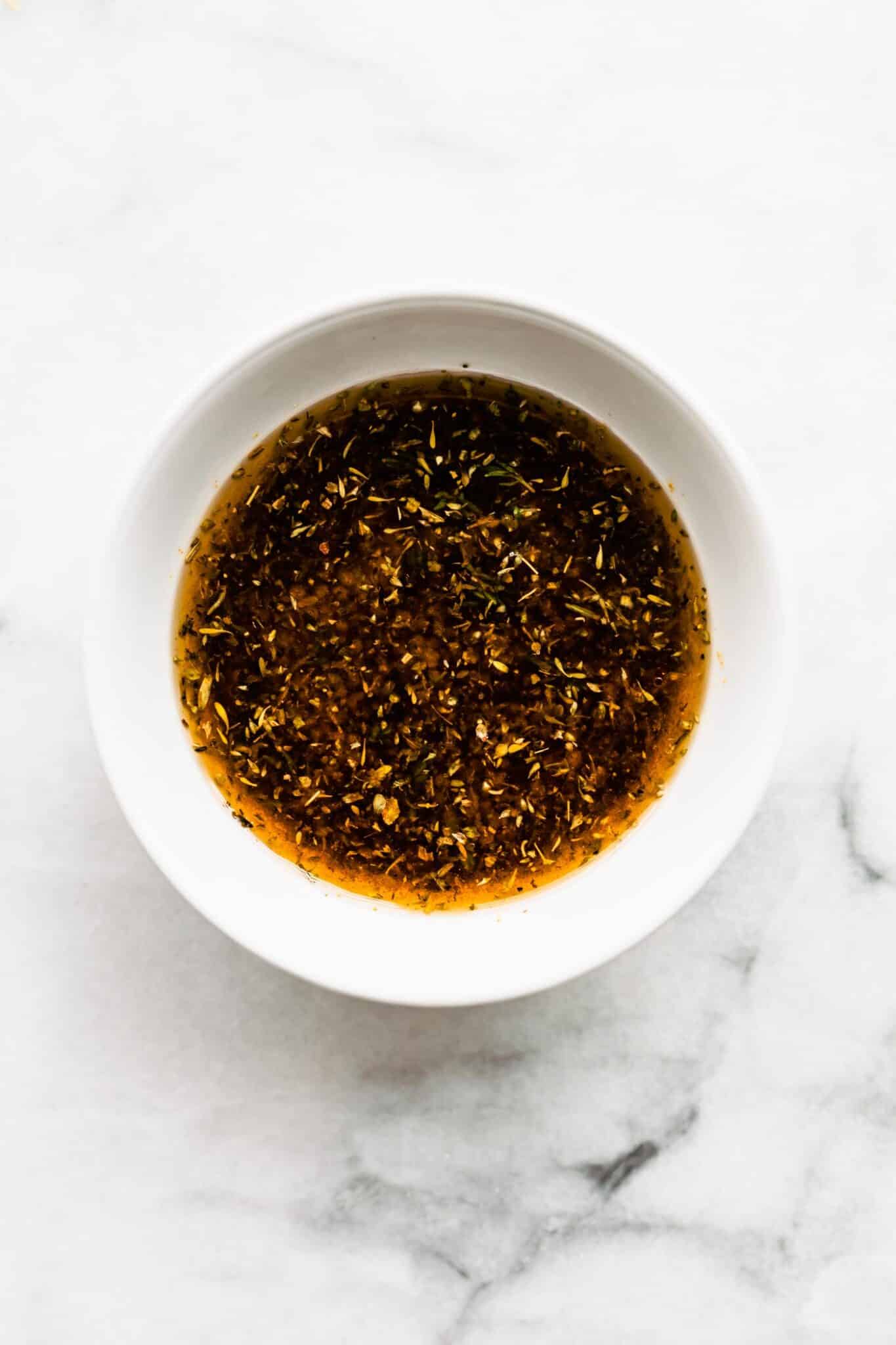 A white bowl filled with a marinade of Greek seasonings and oil.