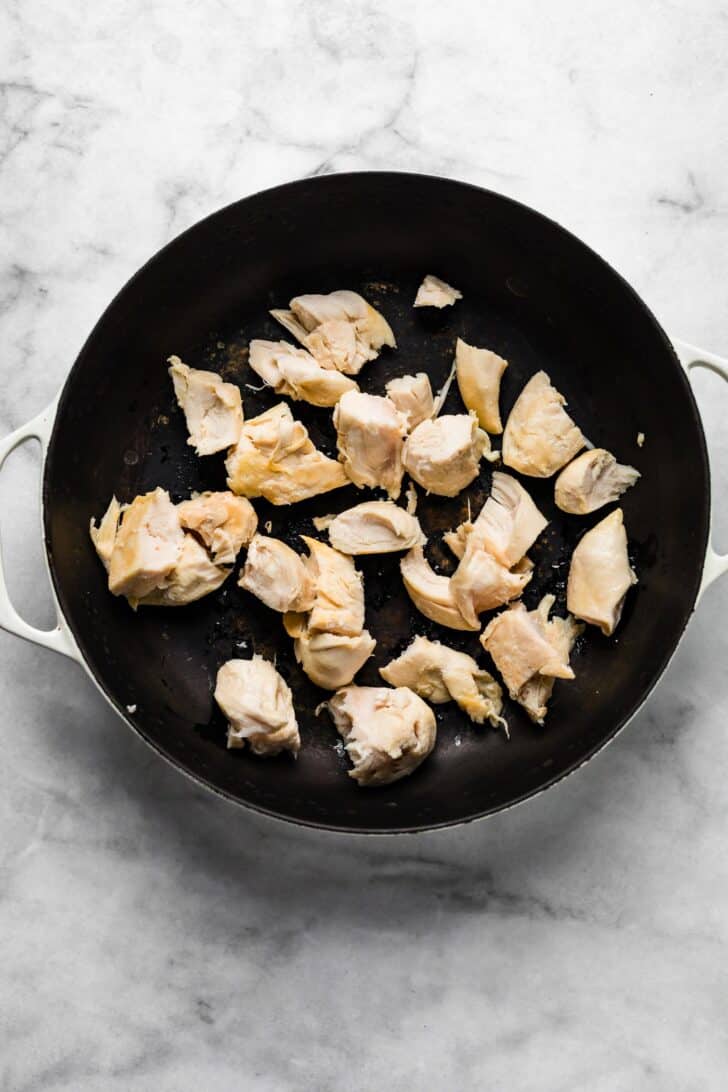 Cooked chunks of chicken breast in a large black skillet, lightly browned