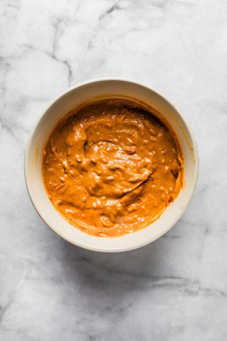 omemade peanut-tomato sauce in a white bowl on a marble surface,