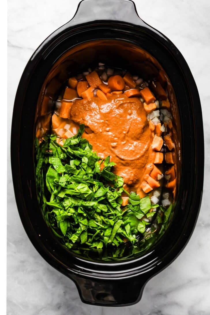 “Chopped spinach and creamy peanut sauce added on top of sweet potatoes and onions in a slow cooker before stirring.