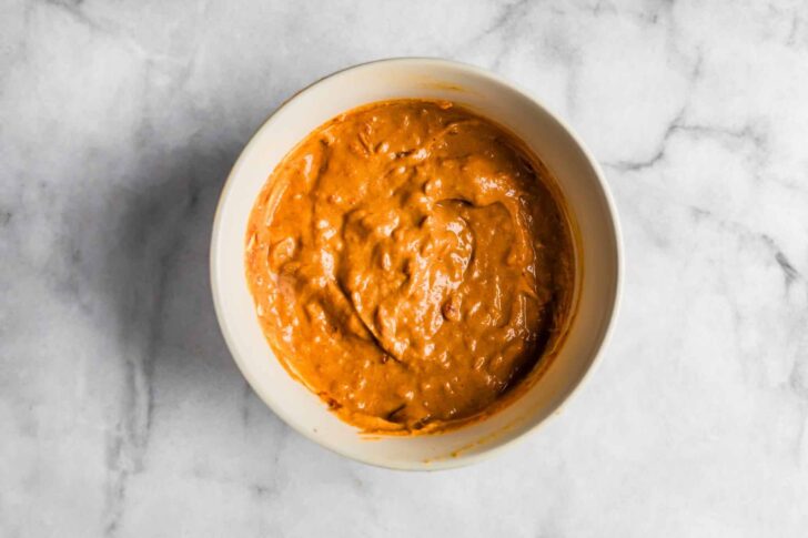 omemade peanut-tomato sauce in a white bowl on a marble surface,