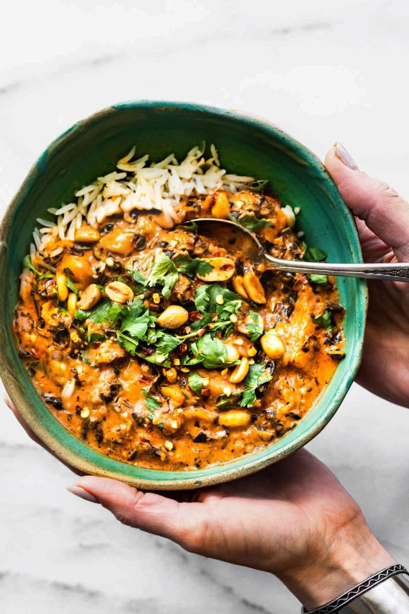 overhead photo: woman's hands holding green bowl of African peanut stew with spoon in bowl