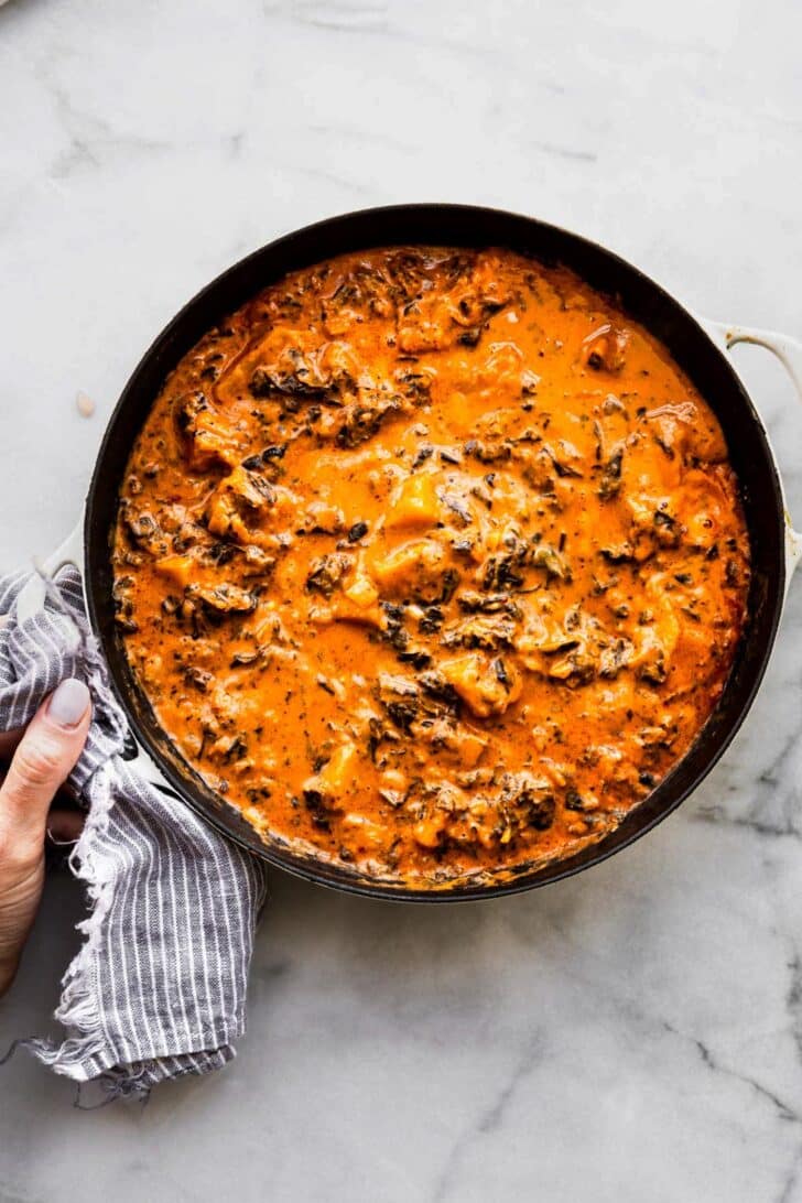 overhead photo: woman's hand using striped kitchen towel to hold handle on pot of stew