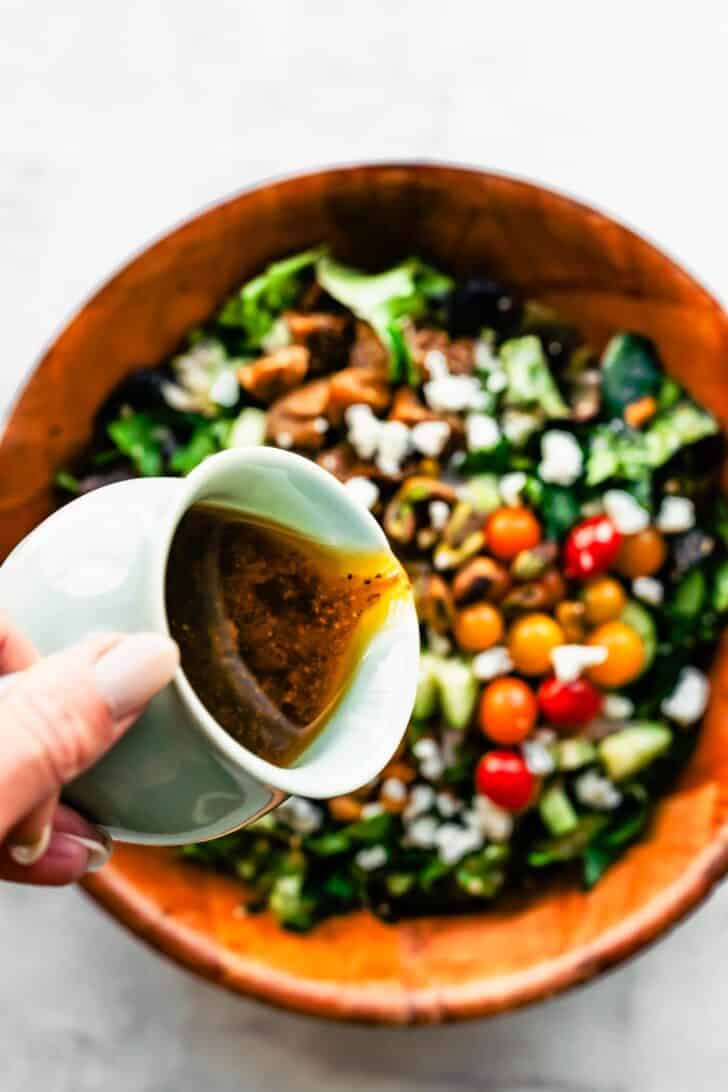 woman's hand pouring dressing over a salad with quinoa and chickpeas and fresh vegetables
