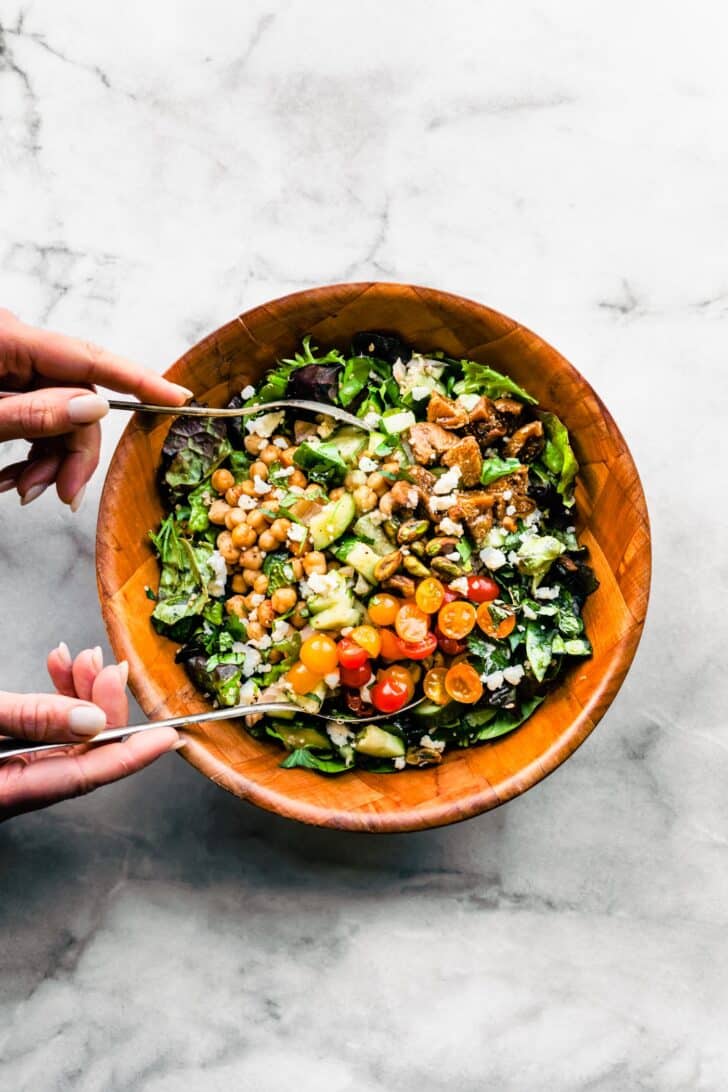 woman's hands tossing a Moroccan salad with quinoa and chickpeas and fresh vegetables in a bowl