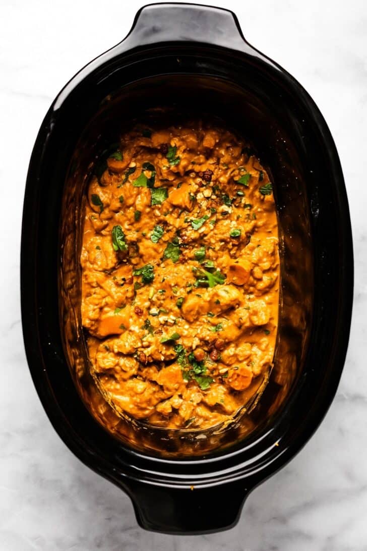 Creamy African peanut stew in a slow cooker garnished with chopped herbs and peanuts