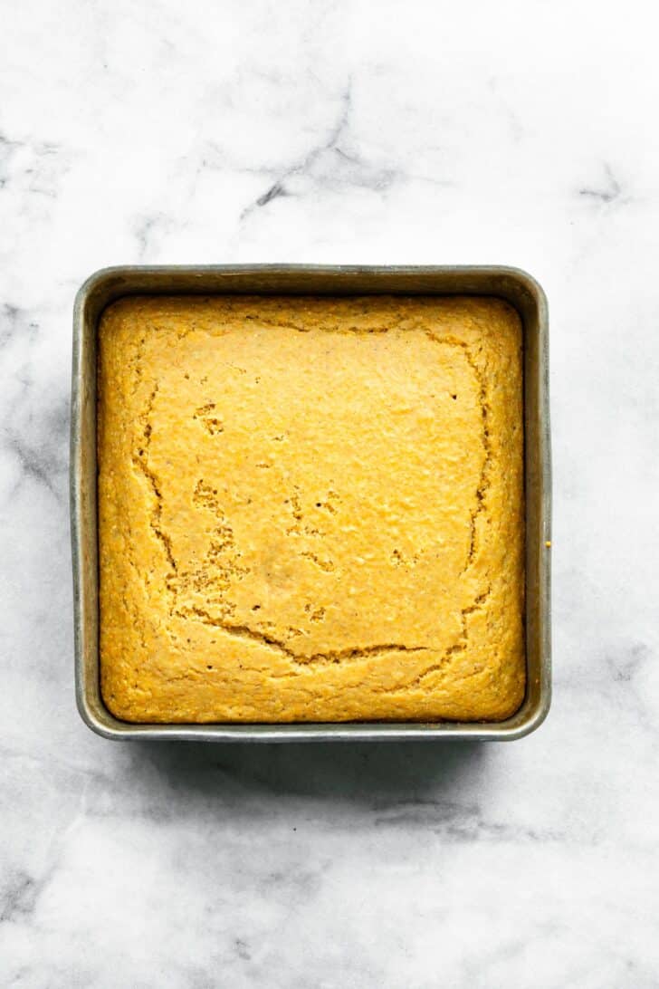 Freshly baked gluten-free cornbread in a square pan with a golden crust and slight cracking on top.
