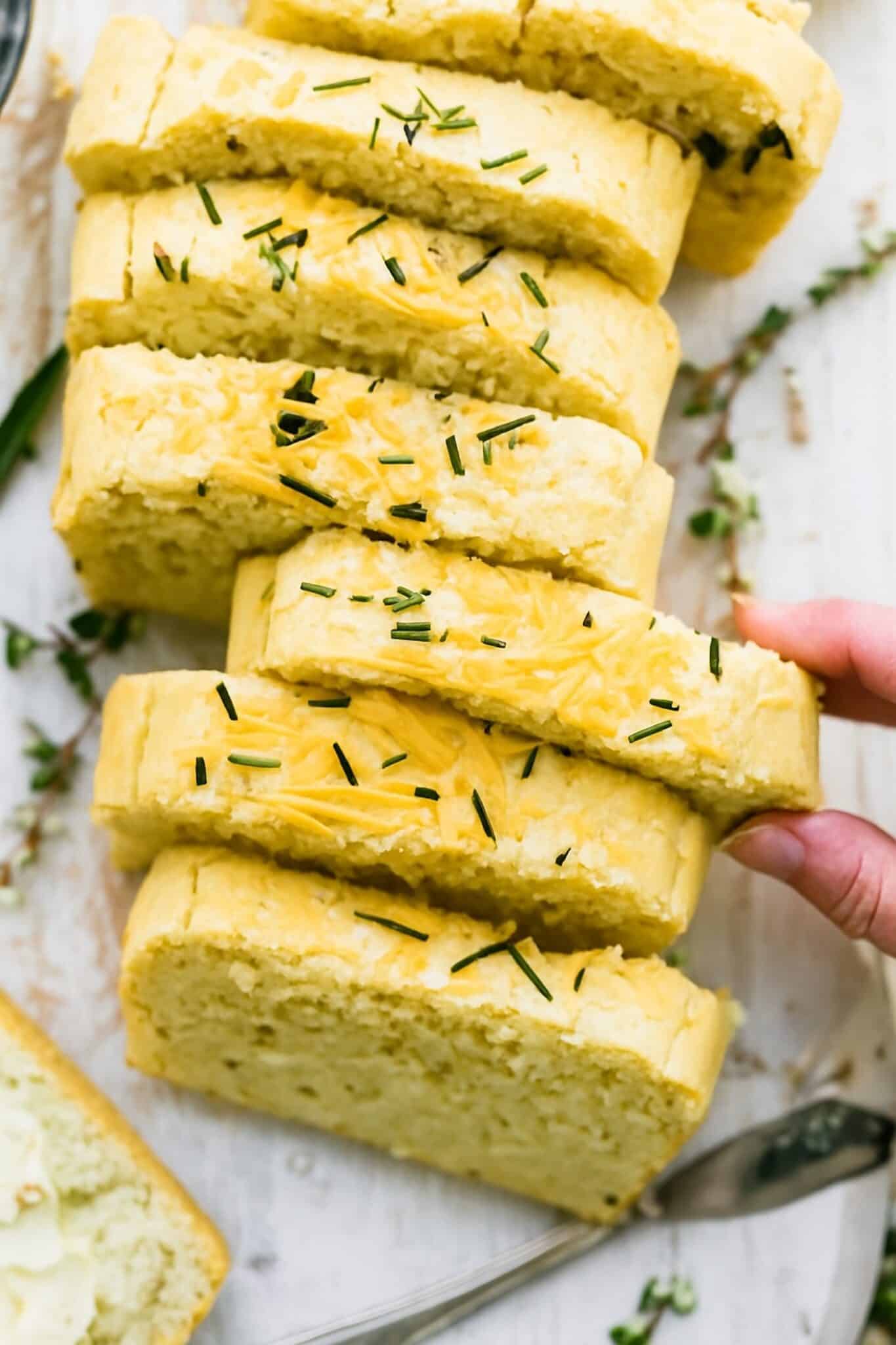 A woman's hand taking a thick slice from homemade loaf of gluten free potato bread.