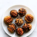 Small no- bake dessert balls drizzled with chocolate and topped with pecans.