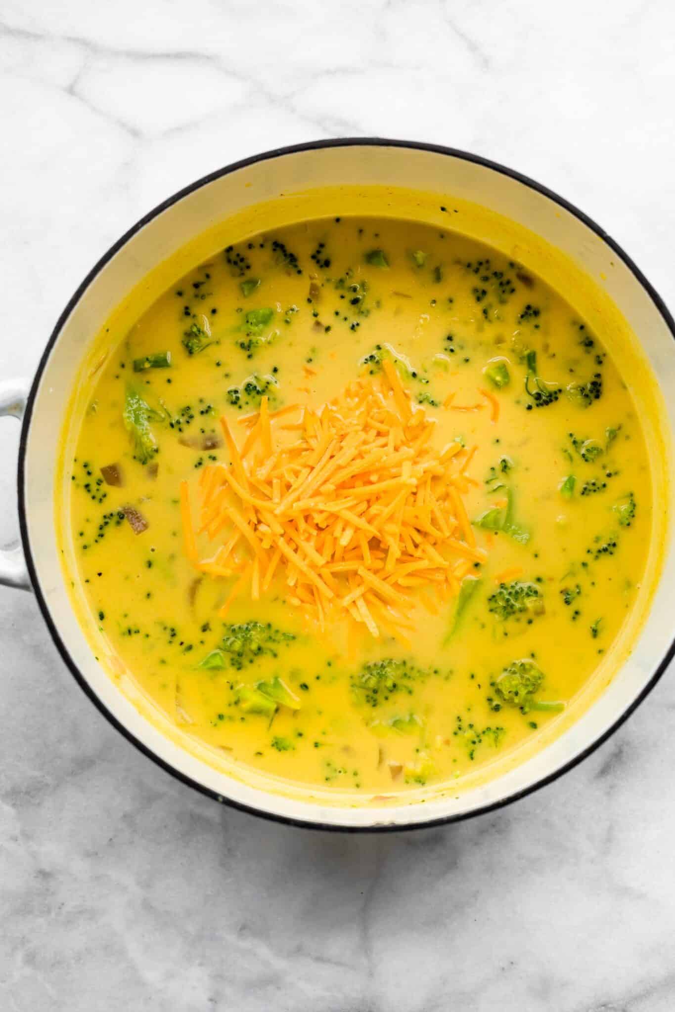 Dairy free broccoli cheese soup in a white Dutch oven with shredded cheese on top.