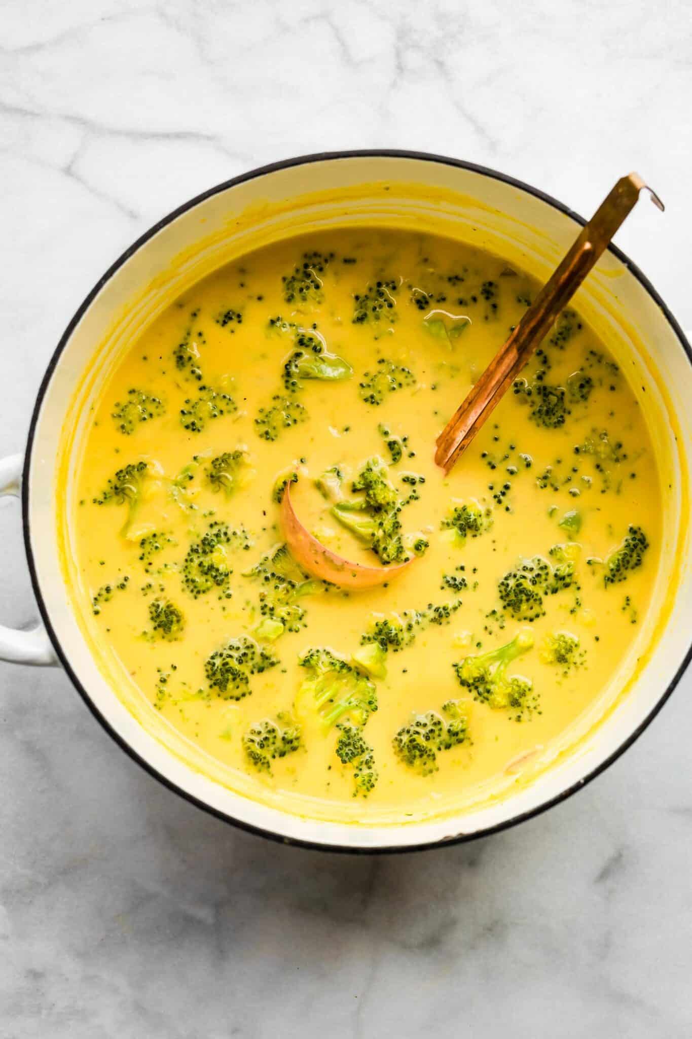 Dairy free broccoli cheese soup in a white Dutch oven with copper ladle in it.