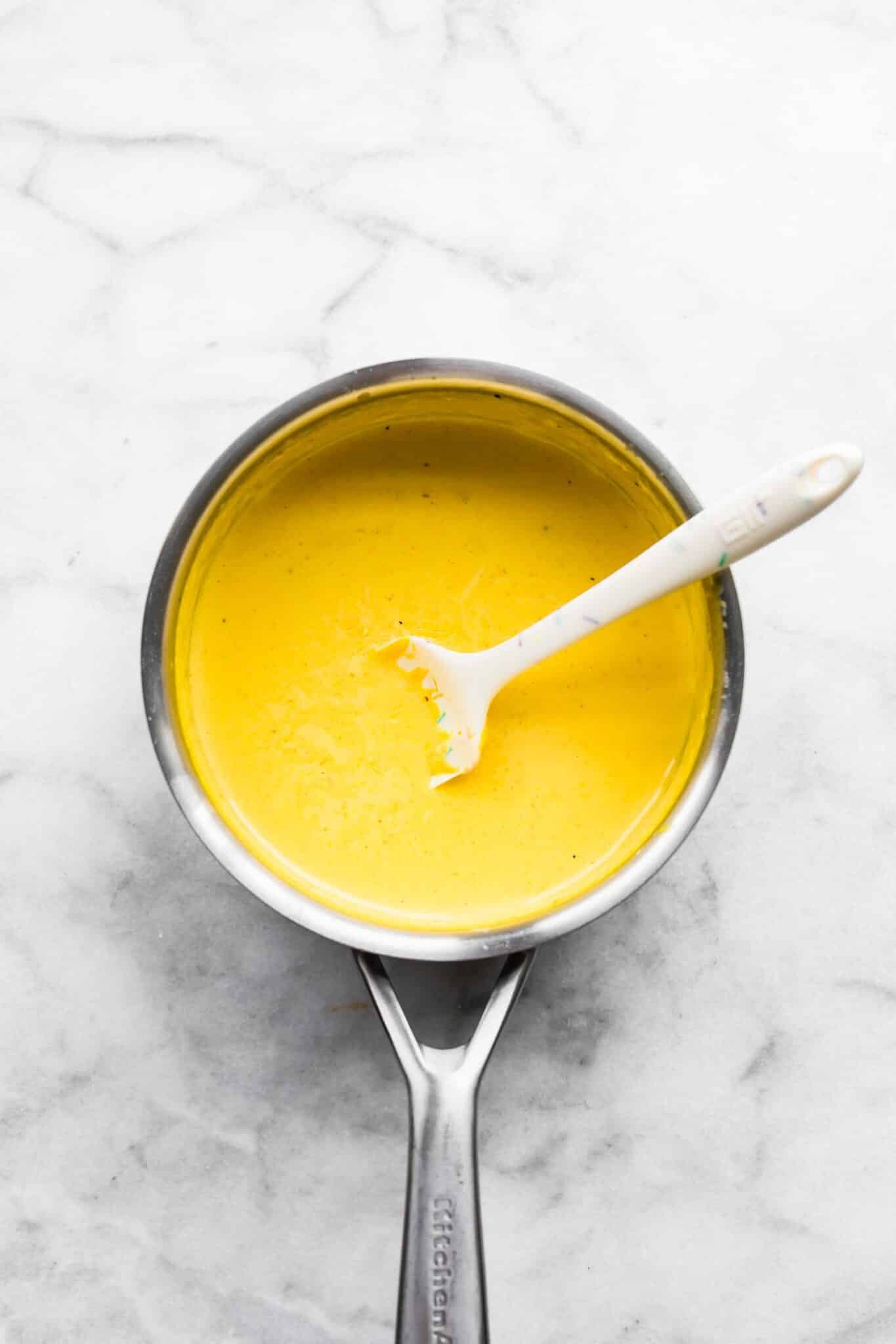 Vegan cheese sauce in a sauce pan with a spatula in it.