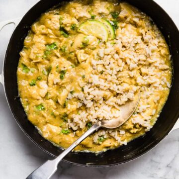 Coconut milk chicken in a cast iron pan with a spoon and rice.