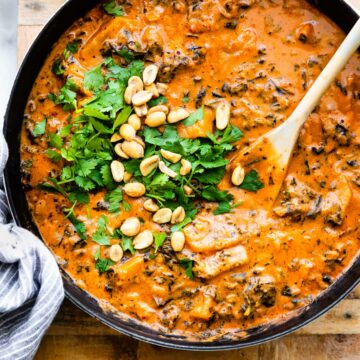 overhead photo: large pot of peanut stew; wooden spoon stirring fresh herbs in