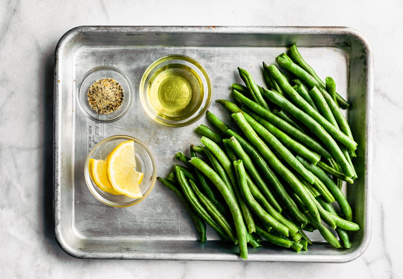 Overhead photo of fresh green beans, oil, lemon and seasonings in a bowl.