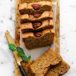 overhead photo of sliced zucchini bread with walnuts on top and knife laying next to it