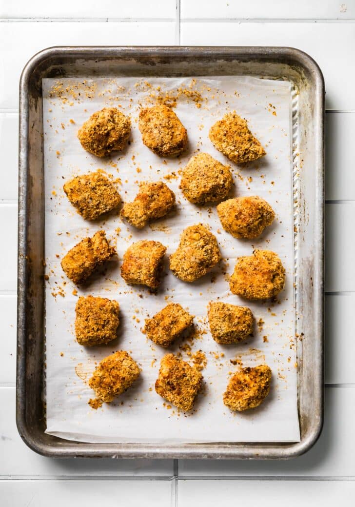 Baked gluten-free chicken nuggets on a parchment-lined tray, golden and crispy.