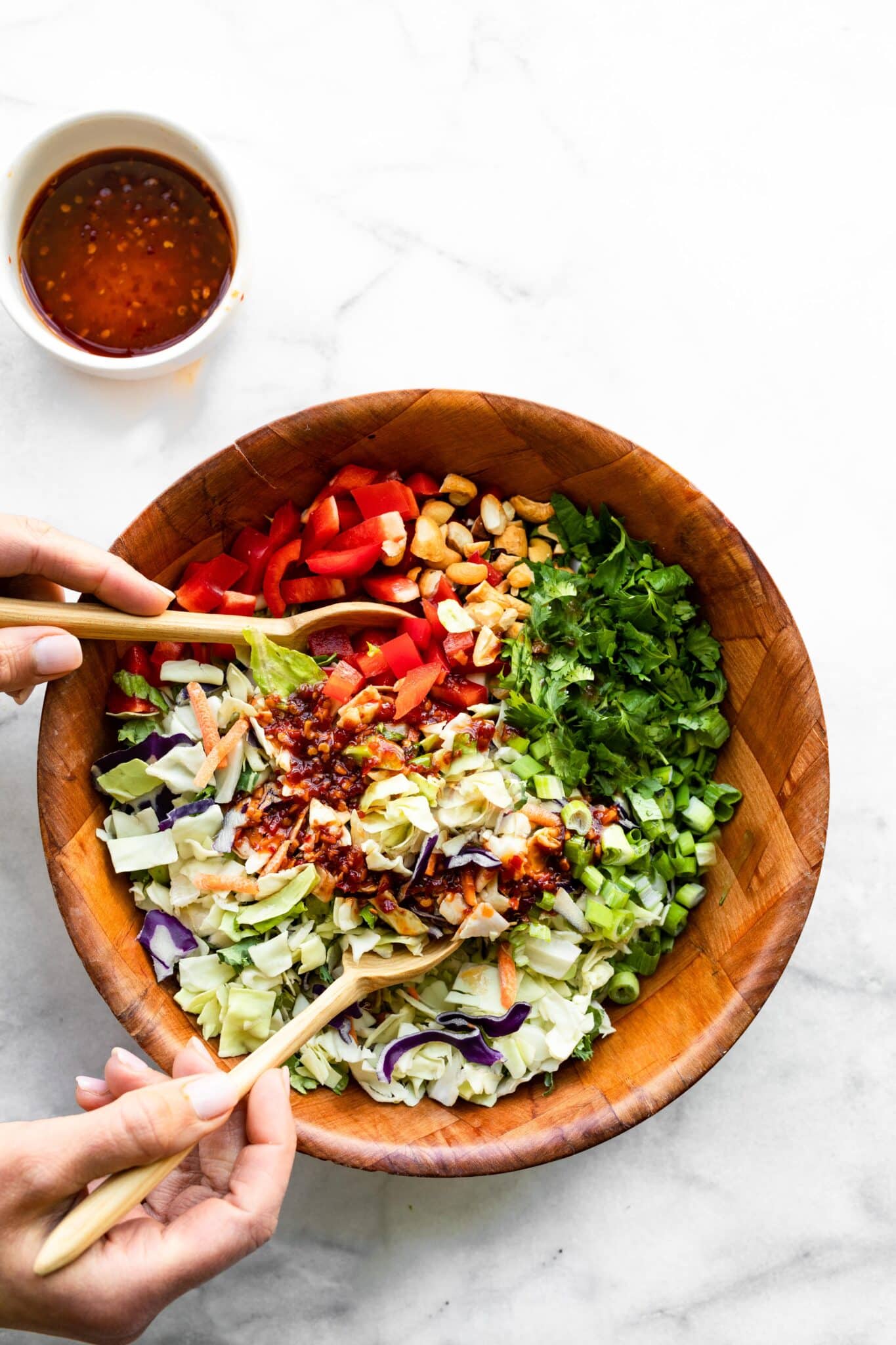 A woman's hands using wooden spoons to mix a Thai noodle salad together.